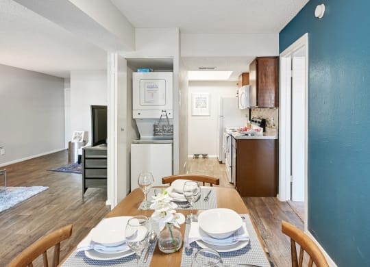 a dining area with a wooden table and chairs and a kitchen in the background