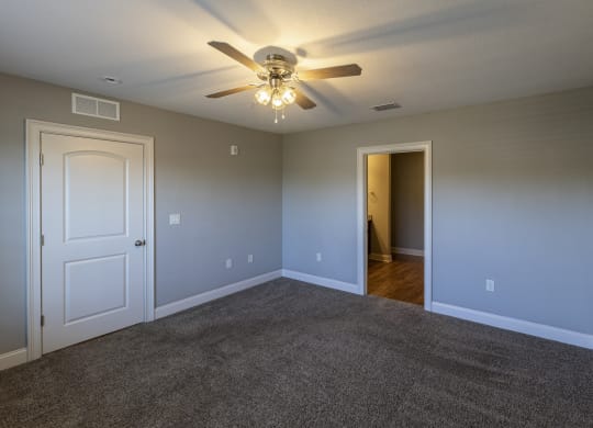 an empty living room with a ceiling fan and a door to a hallway