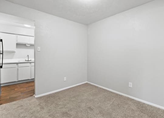 an empty bedroom with a kitchen in the background
