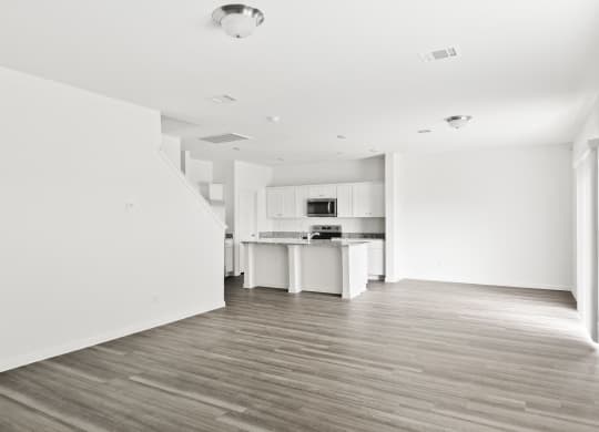 an empty living room and kitchen with white walls and wood floors at Beacon at Bunton Creek, Kyle