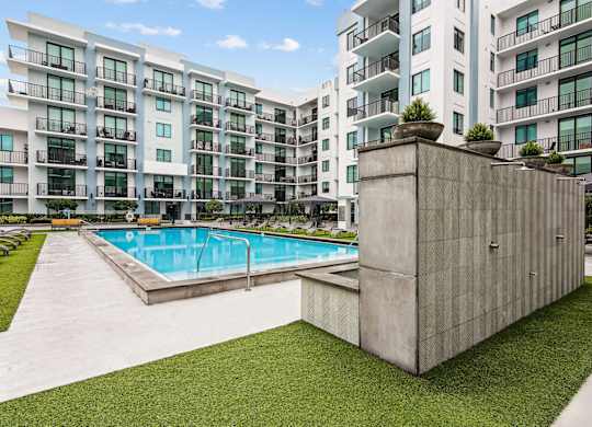 Modern apartment complex with a pool and a small concrete structure with showers at Twenty2 West luxury apartments in Miami, FL.