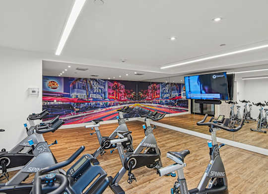 Cycling studio in gym with a row of stationary bikes and a TV at Twenty2 West luxury apartments in Miami, FL