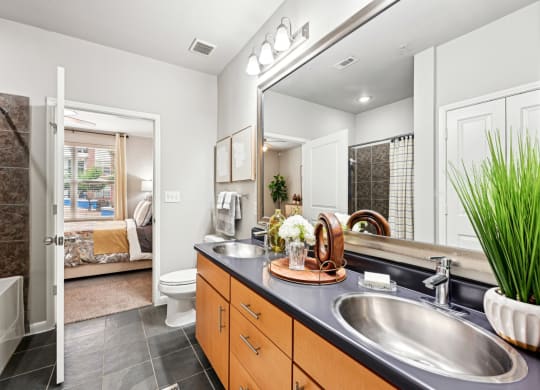 Model apartment master bathroom with a large mirror and a vanity with dual sinks at The Grand at Upper Kirby apartments in Houston, TX