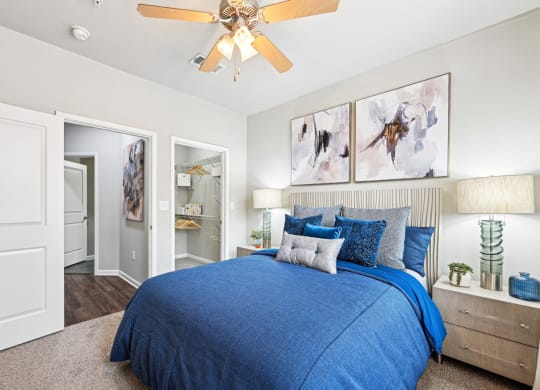 Comfortable bedroom with blue bedding and artistic wall decor at The Grand at Upper Kirby apartments in Houston, TX