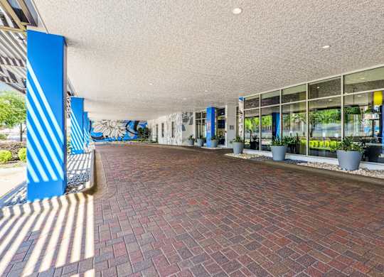 A covered entrance to The Grand at Upper Kirby with a brick road and glass windows in Houston, TX