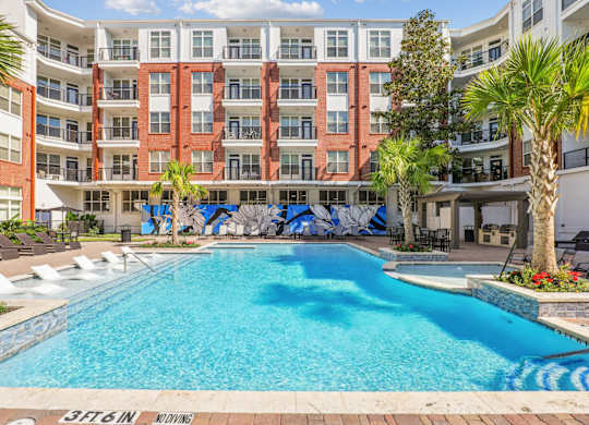 A large swimming pool surrounded by multi-story apartment buildings at The Grand At Upper Kirby in Houston, TX