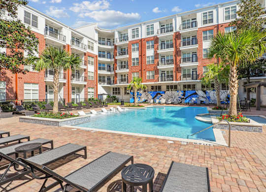 A courtyard pool surrounded by palm trees and lounge chairs at The Grand At Upper Kirby in Houston, TX