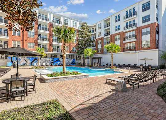 A courtyard pool area with lounge chairs and palm trees at The Grand At Upper Kirby in Houston, TX