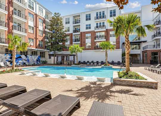 A pool surrounded by lounge chairs and palm trees at The Grand At Upper Kirby in Houston, TX