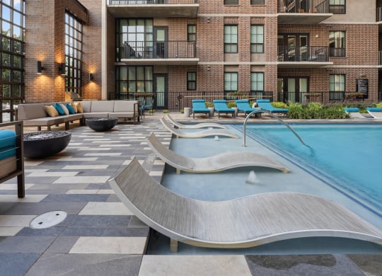 a pool with lounge chairs and a fire pit in front of a brick building