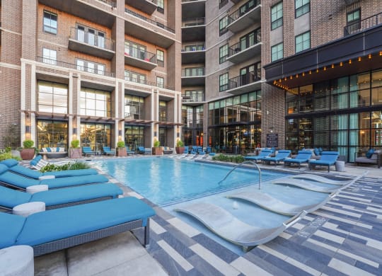 an outdoor swimming pool with chaise lounge chairs in front of an apartment building