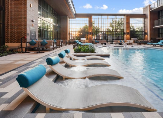 a pool with chaise lounge chairs and a brick building in the background