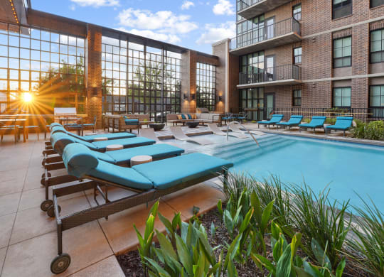 a pool with blue chaise lounge chairs and a brick building in the background