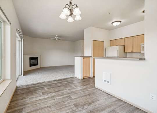 A spacious kitchen with a wooden floor and carpeted living room with a fireplace at The Madison Apartments in Olympia, WA