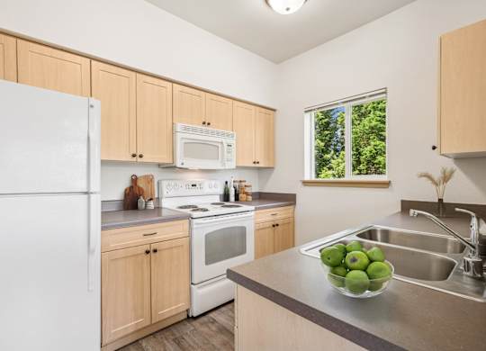 Jackson floor plan kitchen with a white refrigerator, wooden cabinets, and microwave at The Madison apartments in Olympia, WA