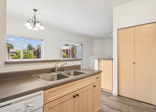 A kitchen with wooden cabinets, a closet, and a sink at The Madison Apartments in Olympia, WA