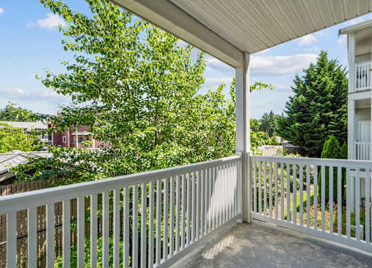 A balcony with white railing overlooking lush trees at The Madison Apartments in Olympia, WA