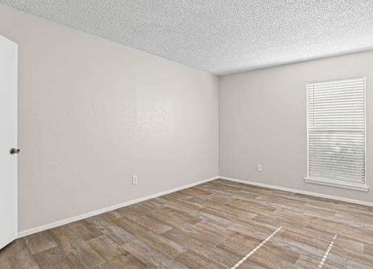 A1 bedroom with wooden flooring and a window with blinds at Vine Apartments in Arlington, TX
