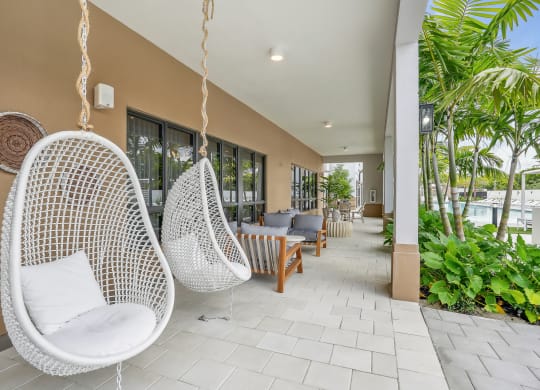 a seating area with hanging chairs and a pool in the background at Westgate on Univeristy in Lauderhill, FL
