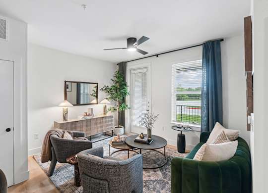 Model living room with a grey couch, a green couch, a coffee table, and a ceiling fan at Whispering Pines at Westdale Hills in Euless, TX