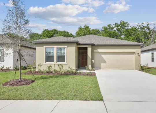 a home with a concrete driveway and a tree in the front yard at Beacon at Woodland Village, Florida
