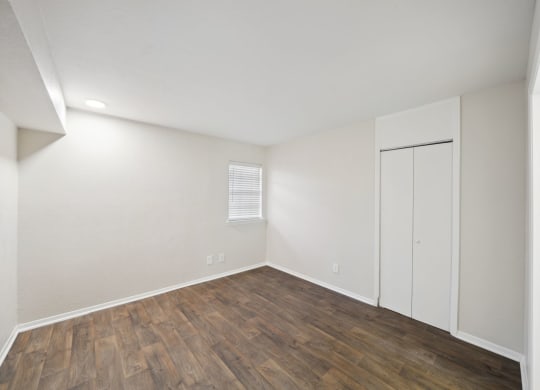 the spacious living room with white walls and wood flooring and a white closet