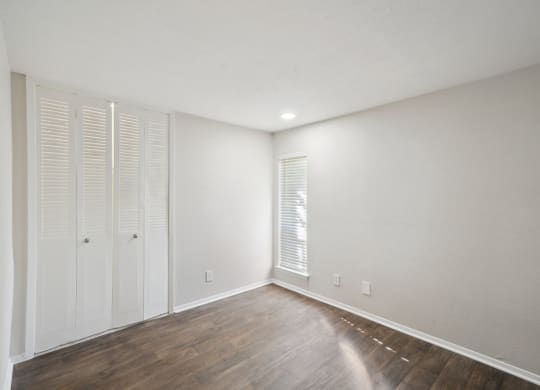 a bedroom with white walls and wood floors and white closet doors