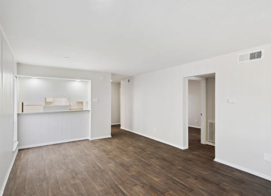 the living room and kitchen of an apartment with white walls and wood floors