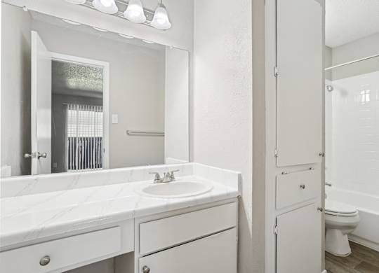 A6 bathroom with a sink, mirror, towel closet, and toilet Windridge on the Parkway apartments in Dallas, TX.