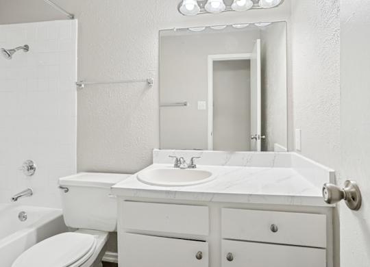 B6 white bathroom with a toilet, sink, and mirror at Windridge on the Parkway in Dallas, TX
