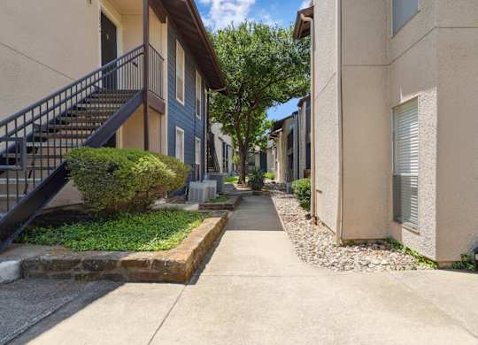 A yellow apartment building exterior and paved walkway at Windridge on the Parkway in Dallas, TX