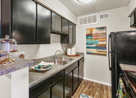 a kitchen with black cabinets, sink and fridge at Bear Creek Crossing apartments in Houston, TX