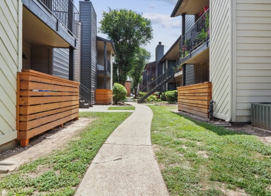 a path between two buildings with a wood fence on the left and a brick building on the