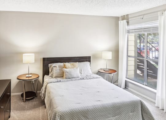 Model apartment second bedroom with a bed, two night stands with lamps, and a window at Hunters Chase Apartments in Austin, TX