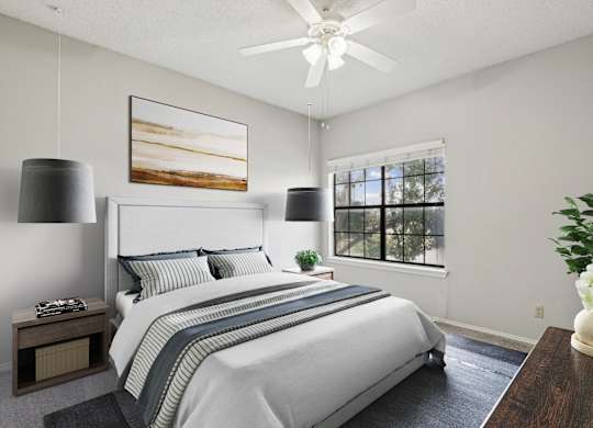 A carpeted bedroom in the B1 floorplan with a large bed, a ceiling fan, and a painting on the wall at Jefferson Creek Apartments in Irving, TX