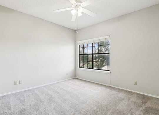 Second bedroom of B1 floor plan with large window and ceiling fan at Jefferson Creek Apartments in Irving, TX.