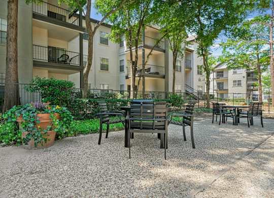 An al fresco dining patio with a table and chairs surrounded by lush trees at Jefferson Place Apartments in Irving, TX