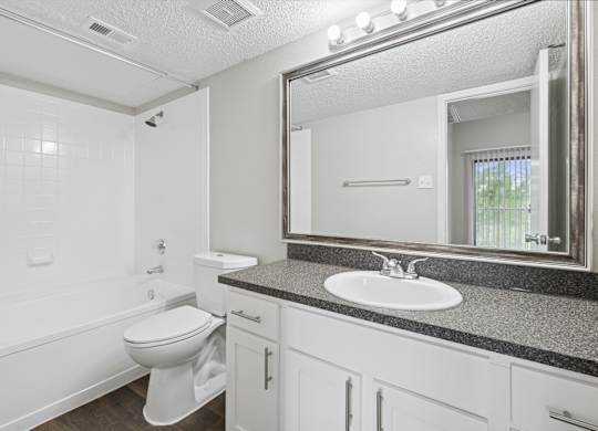 B1 white bathroom with a toilet, sink, vanity lights, and mirror at Jefferson Place Apartments in Irving, TX