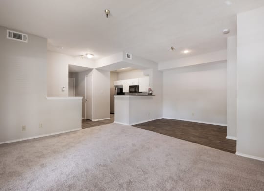 an empty living room with a kitchen in the background