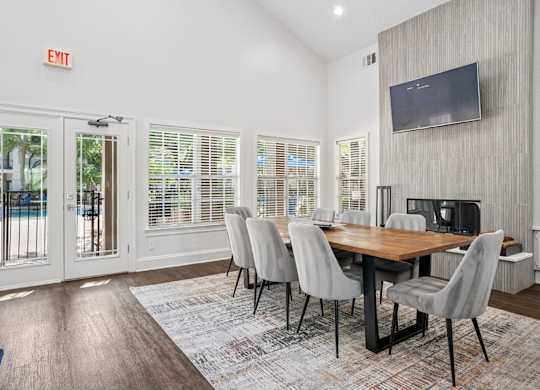 A dining room with a wooden table and chairs, a television on the wall, and a door leading outside.