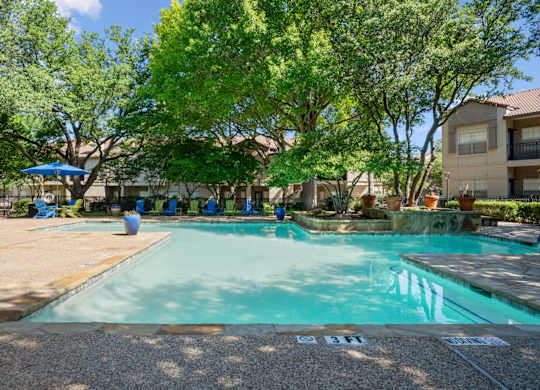 A swimming pool surrounded by trees and green and blue chairs at La Costa in Plano, TX.
