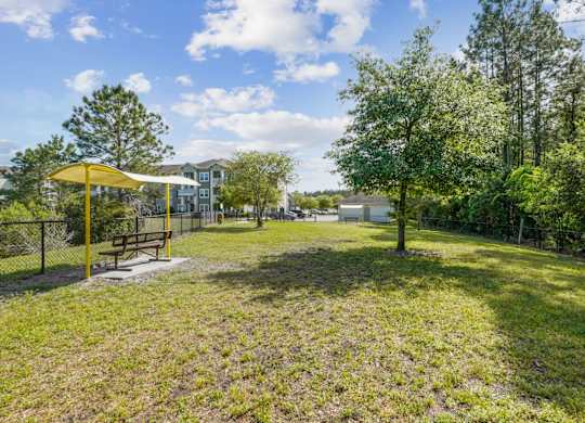 A park with a yellow umbrella and a bench.