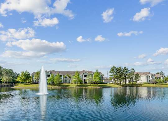 A fountain in the middle of a lake with houses in the background.