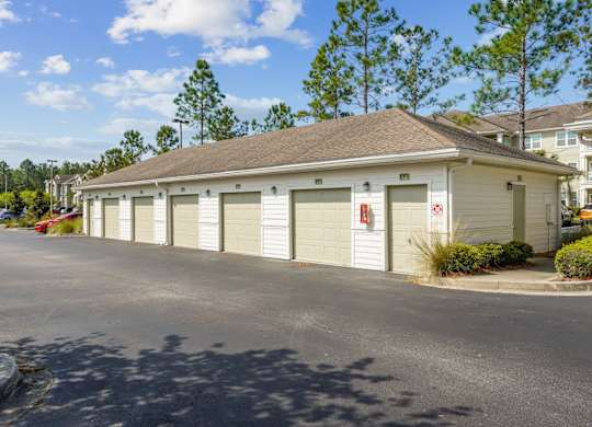 A building with a grey roof and white garage doors is surrounded by a parking lot.