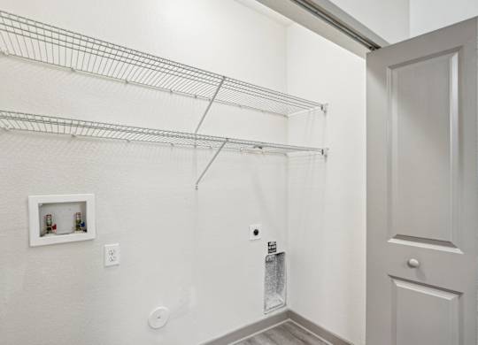 A laundry closet with washer and dryer connections and shelving at Oakleaf Plantation apartments in Jacksonville, FL.