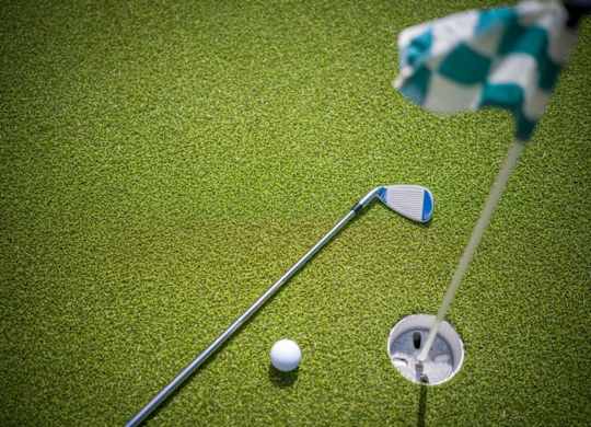 A golf ball is on the ground near a hole with a flag and a club.