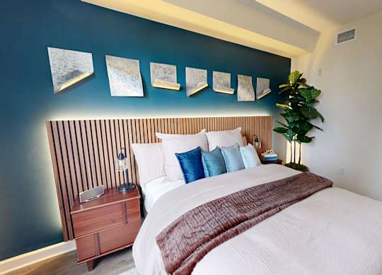A bedroom with a bed, pillows, a nightstand, and a plant.