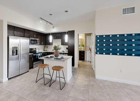 A kitchen with a refrigerator, stove, and bar stools.