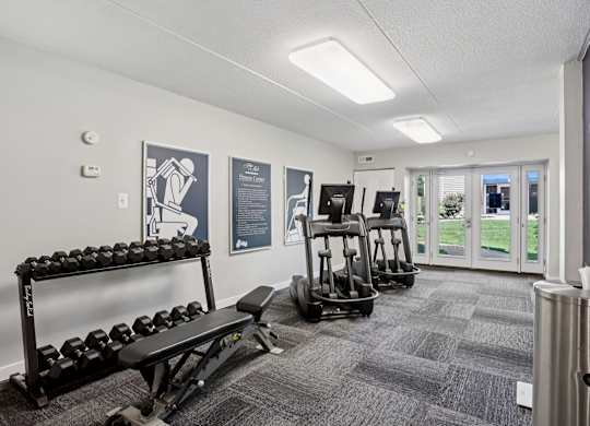 A gym with a variety of equipment including dumbbells, a bench, and a rowing machine.