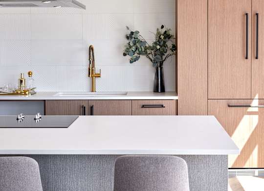 A modern kitchen with a white countertop and grey bar stools.